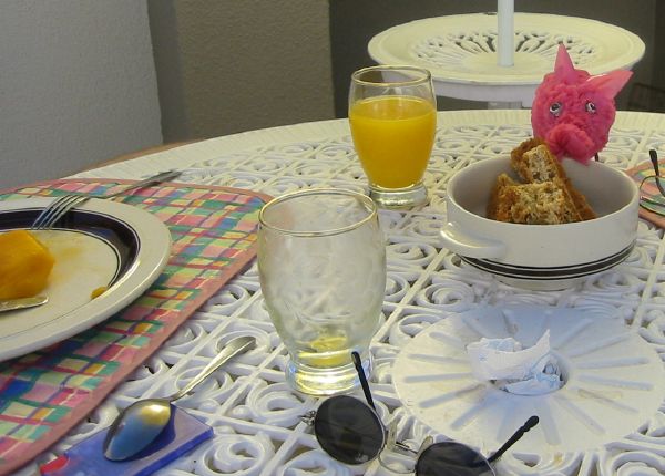 Breakfast table on the balcony with mango, orange juice and a pink pig eating rusks