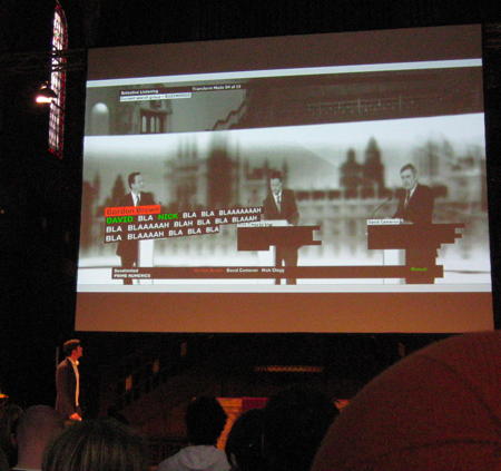 Justin Manor speaking at see conference 2011 with a screen from their project analysing election campaign discussions in the U.K. in the background: the key words are highlighted, the rest is transformed to 'bla'